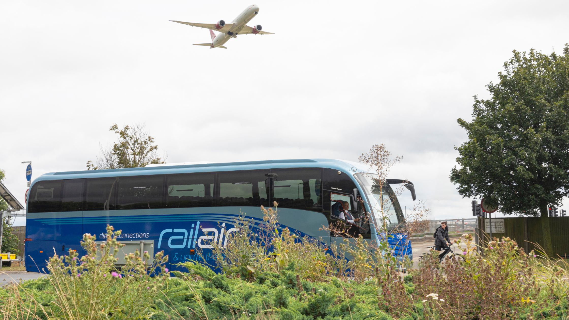 Image of RailAir bus service RA3 driving away from Heathrow with a flight taking off nearby